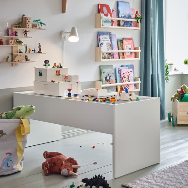 Eine weiße Wandleuchte beleuchtet einen weißen, großzügigen Spieltisch mit Stauraum. BYGGLEK LEGO®-Steine und -Schachteln befinden sich auf der Tischplatte.
