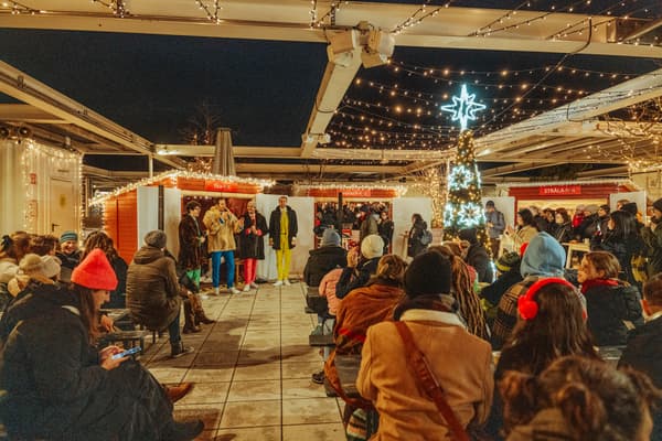 Eine Winterlich gekleidete Personengruppe hört einer Rede auf einem Weihnachtsmarkt zu.