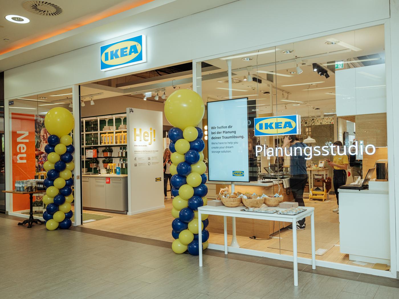 Eingangsbereich eines IKEA Planungsstudios mit gelb-blauer Ballondekoration, Informationsmonitor und Snacks auf einem Tisch