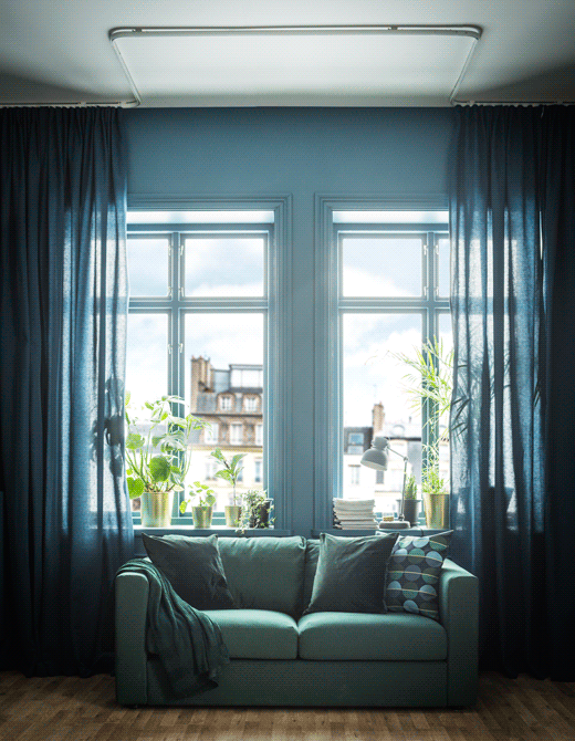 El GIF muestra unas cortinas azules que van del suelo al techo y que se colocan alrededor de un sofá para aportar privacidad.