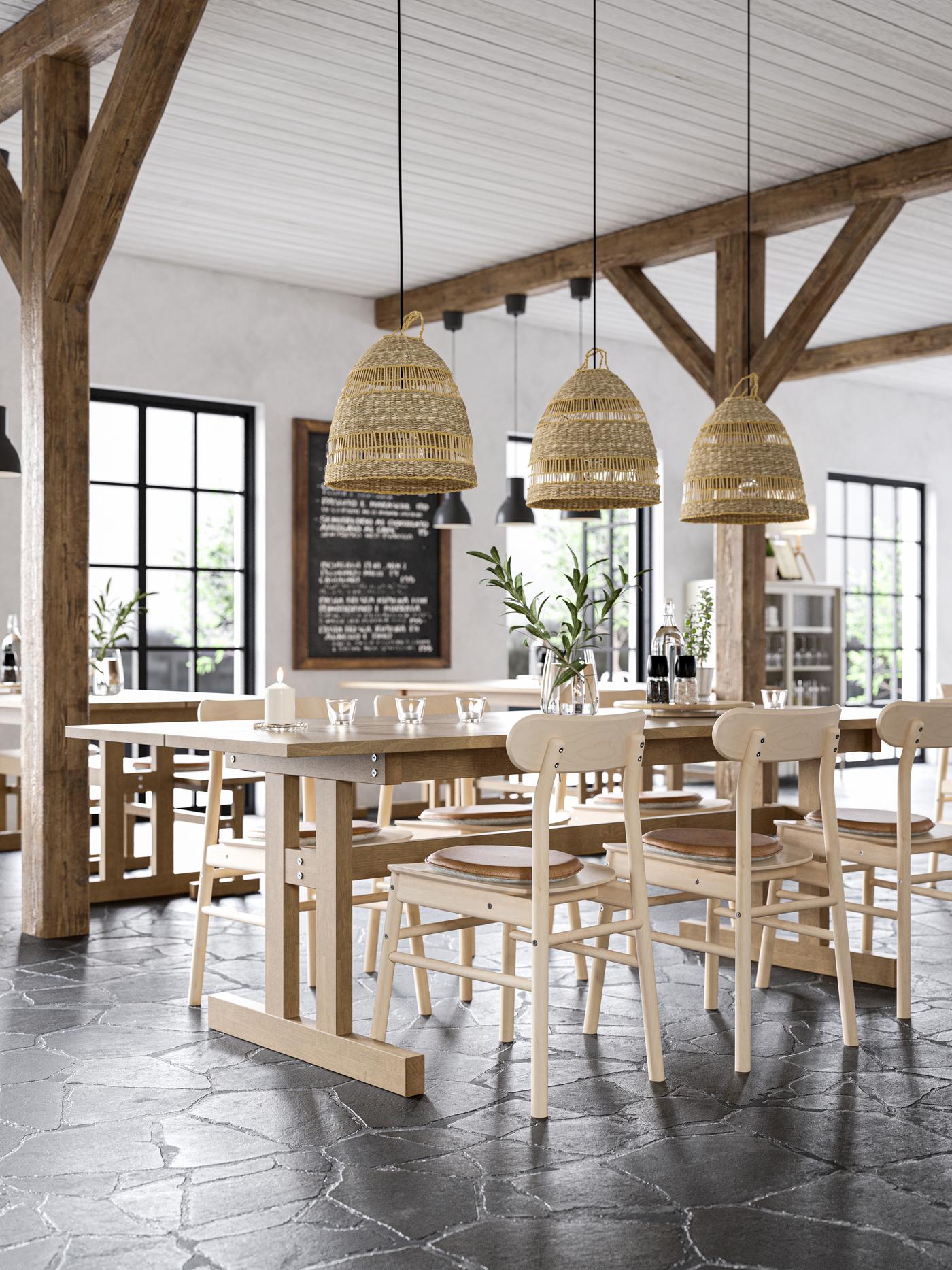 El interior de un café con grandes vigas de madera en el techo y lámparas colgantes de mimbre. También hay mesas y silas altas de madera IKEA.