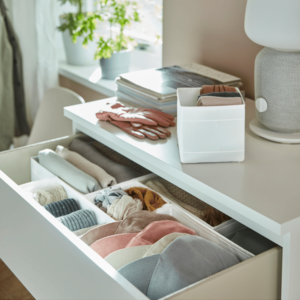 El primer cajón de una cómoda blanca abierto, donde se muestran accesorios de vestir ordenados con divisores interiores blancos. 
