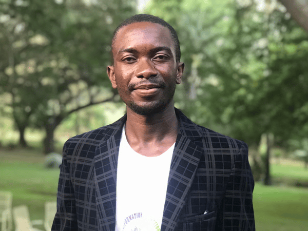 El refugiat congolés Barthelemy Mwanza mira a la cámara, sonríe y viste una chaqueta negra y una camiseta blanca.