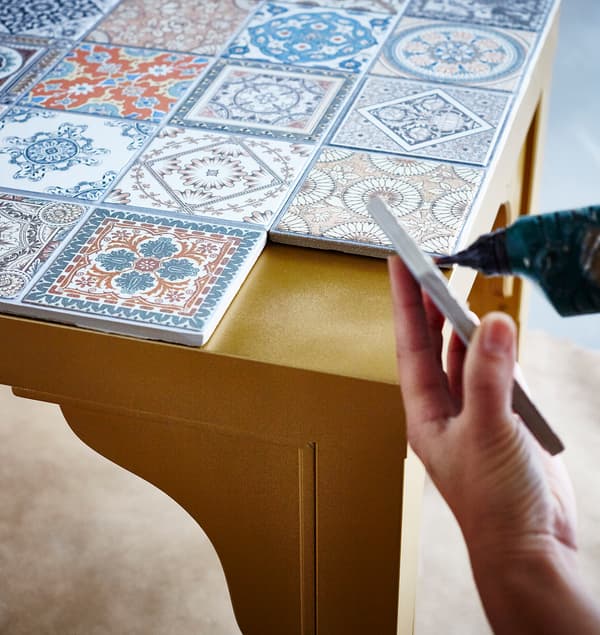 El tablero de una mesa IKEA LACK dorada que están decorando con una variedad de azulejos decorativos.
