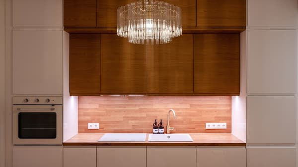 Elegant contemporary kitchen with warm wood cabinetry, integrated appliances, soft ambient lighting, and a statement crystal pendant light creating a refined and welcoming atmosphere.