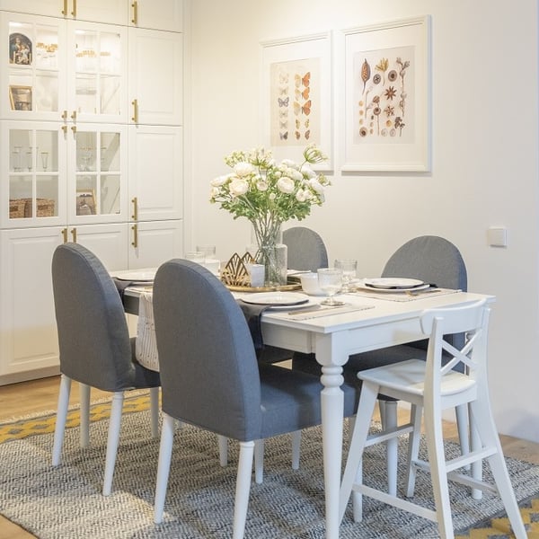 Elegant dining room with white table, grey chairs, and flower centerpiece.