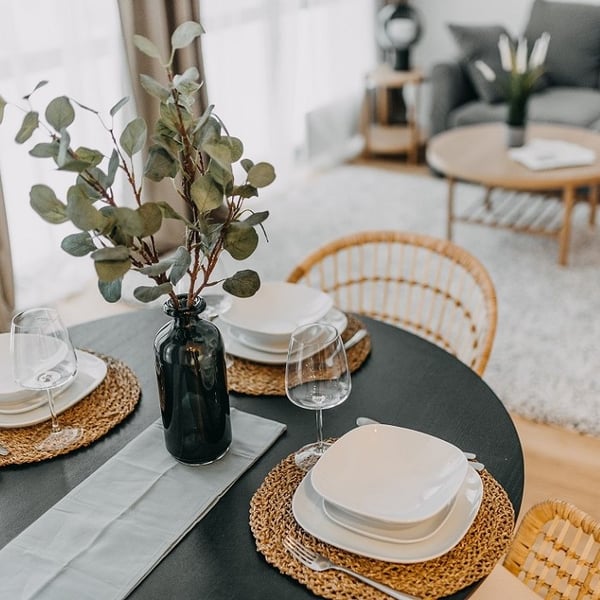 Elegant dining table setting with white plates, wine glasses, and a black vase centerpiece.