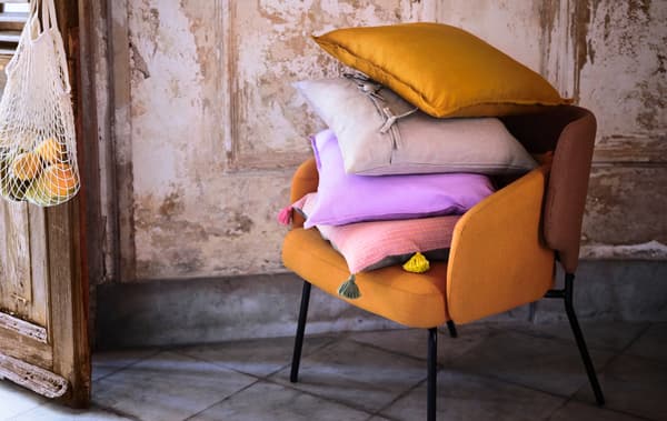 Elegant innredning med rustikke naturmaterialer. I en lenestol ligger det en stabel puter, en av dem med et KLARAFINA putetrekk.