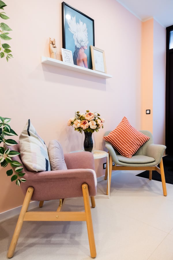 Elegant salon corner with pink and green chairs, wall art, and a vase of roses.