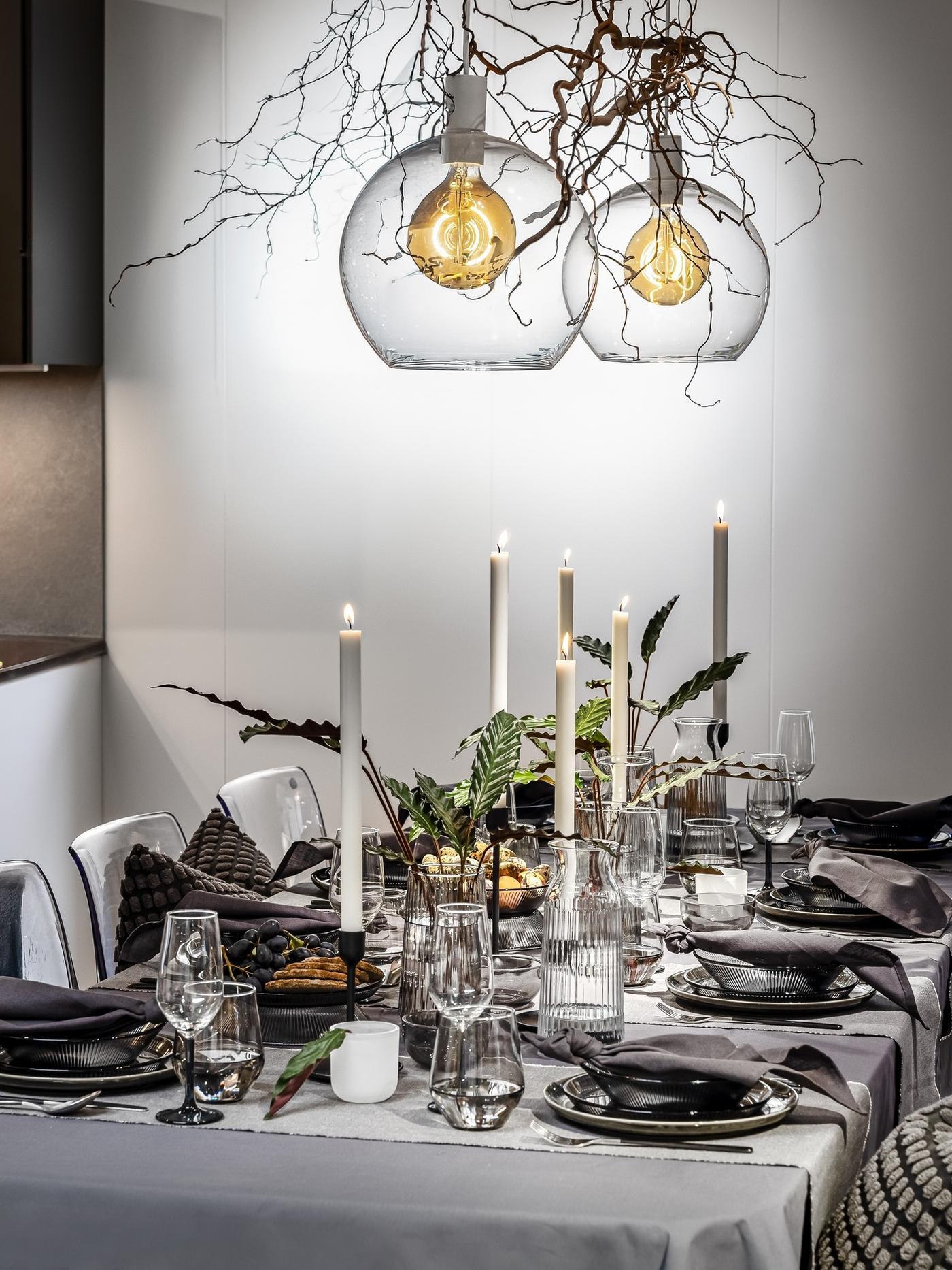 Elegant table arrangement with textured grey linens, black candle holders and simple greenery in small vases.