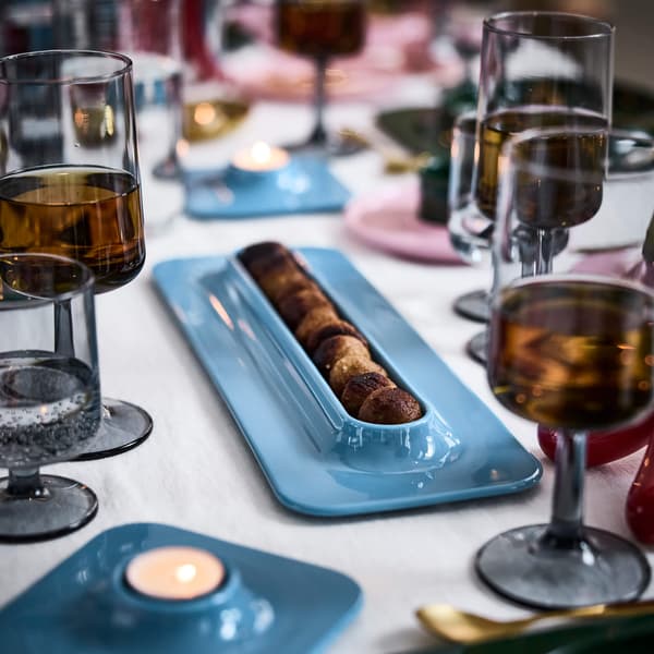 Elegant table with glasses of amber drink, blue tray of meatballs, and glowing tealight candles creating a warm ambiance.