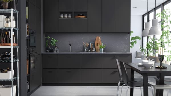 Elegantná kuchyňa so skrinkami v antracitovej farbe, tmavosivými stenami a čiernym jedálenským stolom a stoličkami.