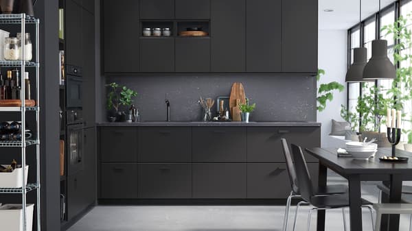 Elegantná kuchyňa so skrinkami v antracitovej farbe, tmavosivými stenami a čiernym jedálenským stolom a stoličkami.