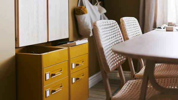 Éléments muraux IVAR et caissons à tiroirs IDÅSEN sur roulettes, table et deux chaises, et sacs accrochés au mur.
