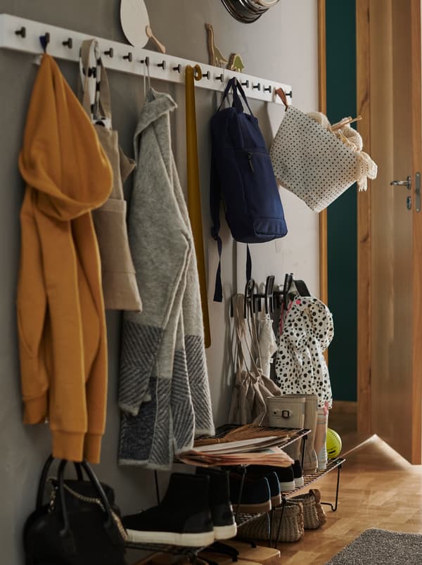 Előszoba három fekete GREJIG cipőtartóval és három fehér LURT állványra felakasztott kabátokkal és táskákkal.