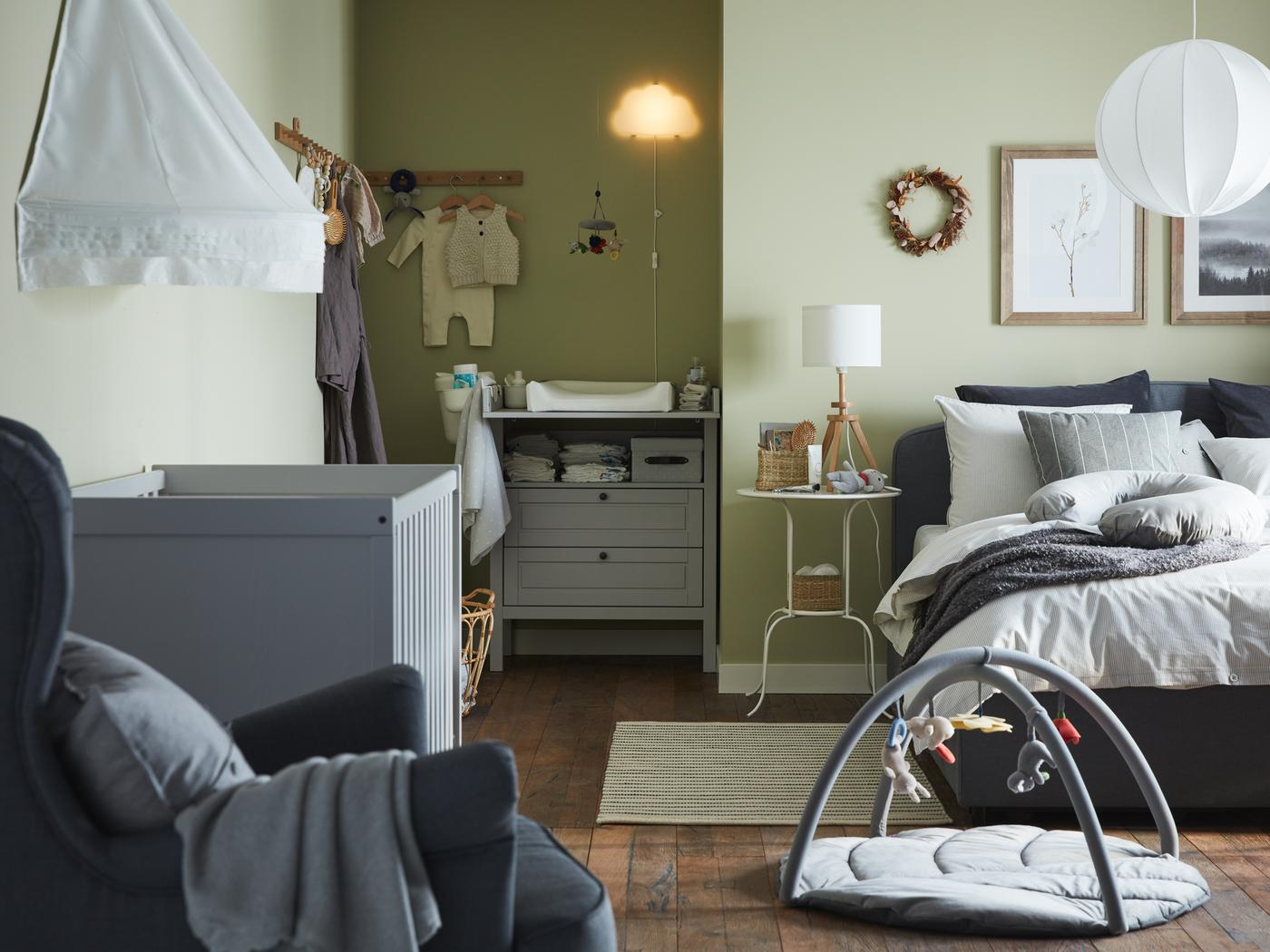 Eltern-Kind-Schlafzimmer mit einem grauen Polsterbett, einem grauen Babybett, einem grauen Wickeltisch/Kommode und grünen Wänden.