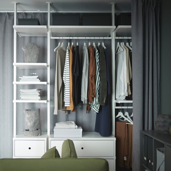 ELVARLI opbergsysteem met witte kleerhangers, tijdschriften en decoratieve artikelen. Vooraan zit een grijs gordijn die het kan bedekken.
