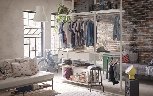ELVARLI storage system filled with clothing and books in an apartment with exposed brick.