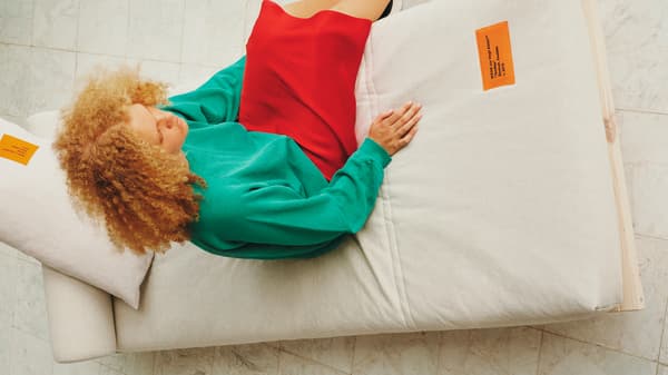 Emakume bat eroso dago koltxoi gris koloreko egurrezko sofa-ohe batean etzanda.