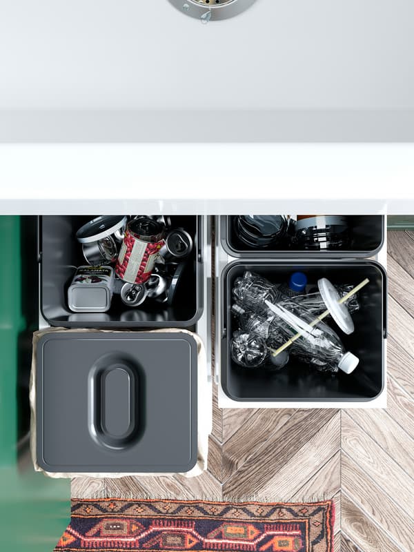 Empat tong pengasingan sampah VARIERA IKEA berwarna hitam berisi botol plastik dan tin kosong. Salah satu tong mempunyai penutup di atasnya.