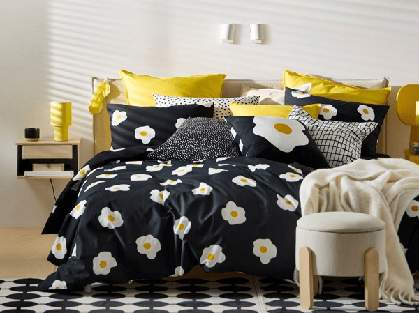 En bäddad säng med blommönster. Kuddarna är gula och framför sängen står en pall.