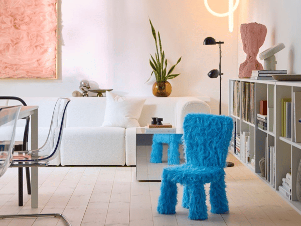 En barnstol i ett ljusblått, luddigt tyg står i ett ljust och vitmålat rum, vit soffa och vit bokhylla med ljust trägolv.  