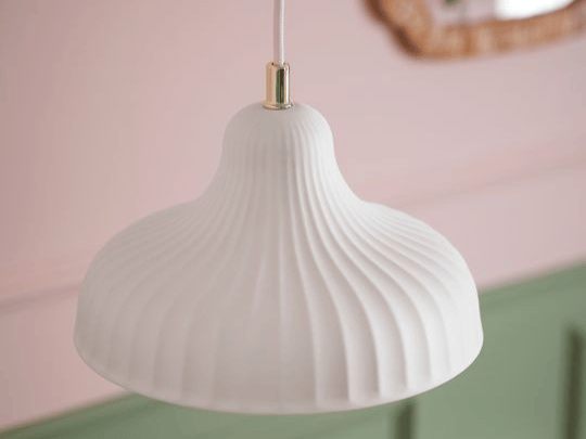 En bild på en taklampa i vitt glas som hänger mot en grön och rosa vägg som bakgrund.