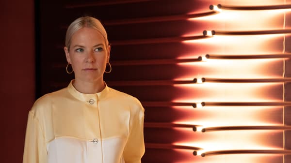 En blond kvinna i gul och vit blus står framför en vägglampa