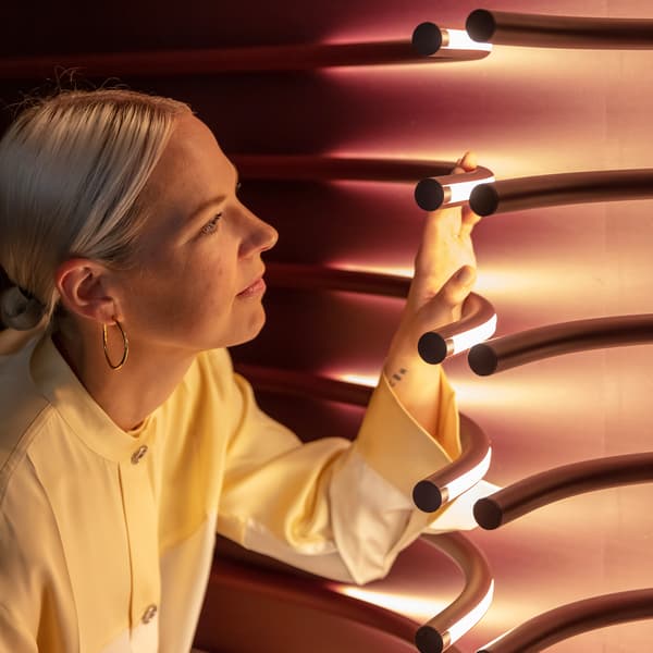 En blond kvinna rör vid en linjeformad vägglampa. 