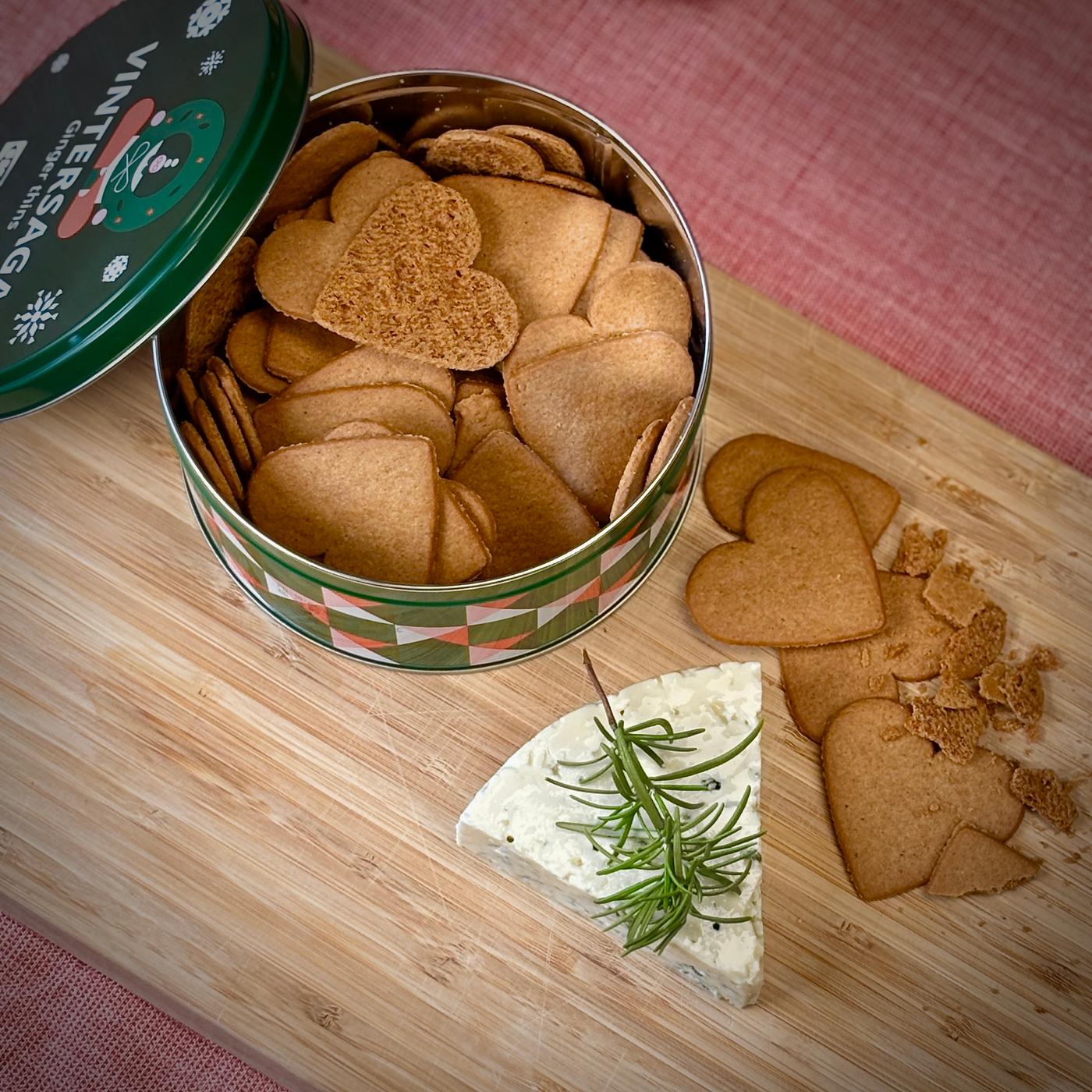 En dåse med hjerteformede brunkager står på et skærebræt ved siden af en blåskimmelost.