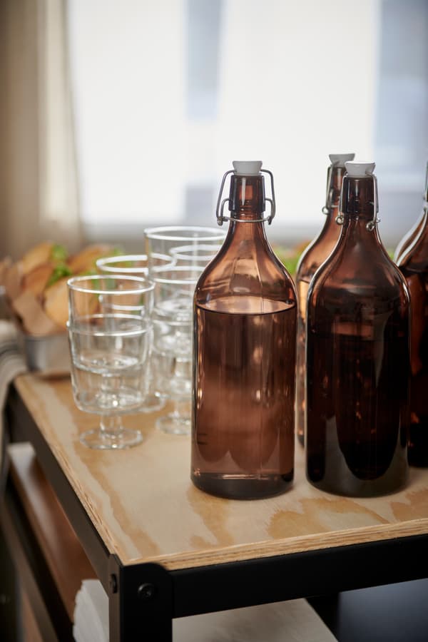 En detaljbild på mörkbruna flaskor och genomskinliga glas som står på en serveringsvagn. 