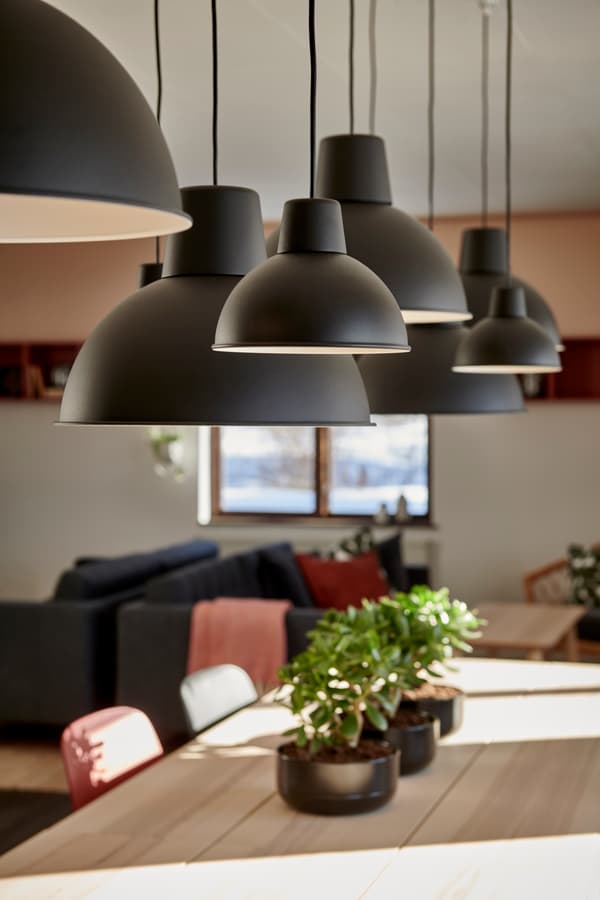 En detaljbild på svarta taklampor som hänger över ett långt matbord. 