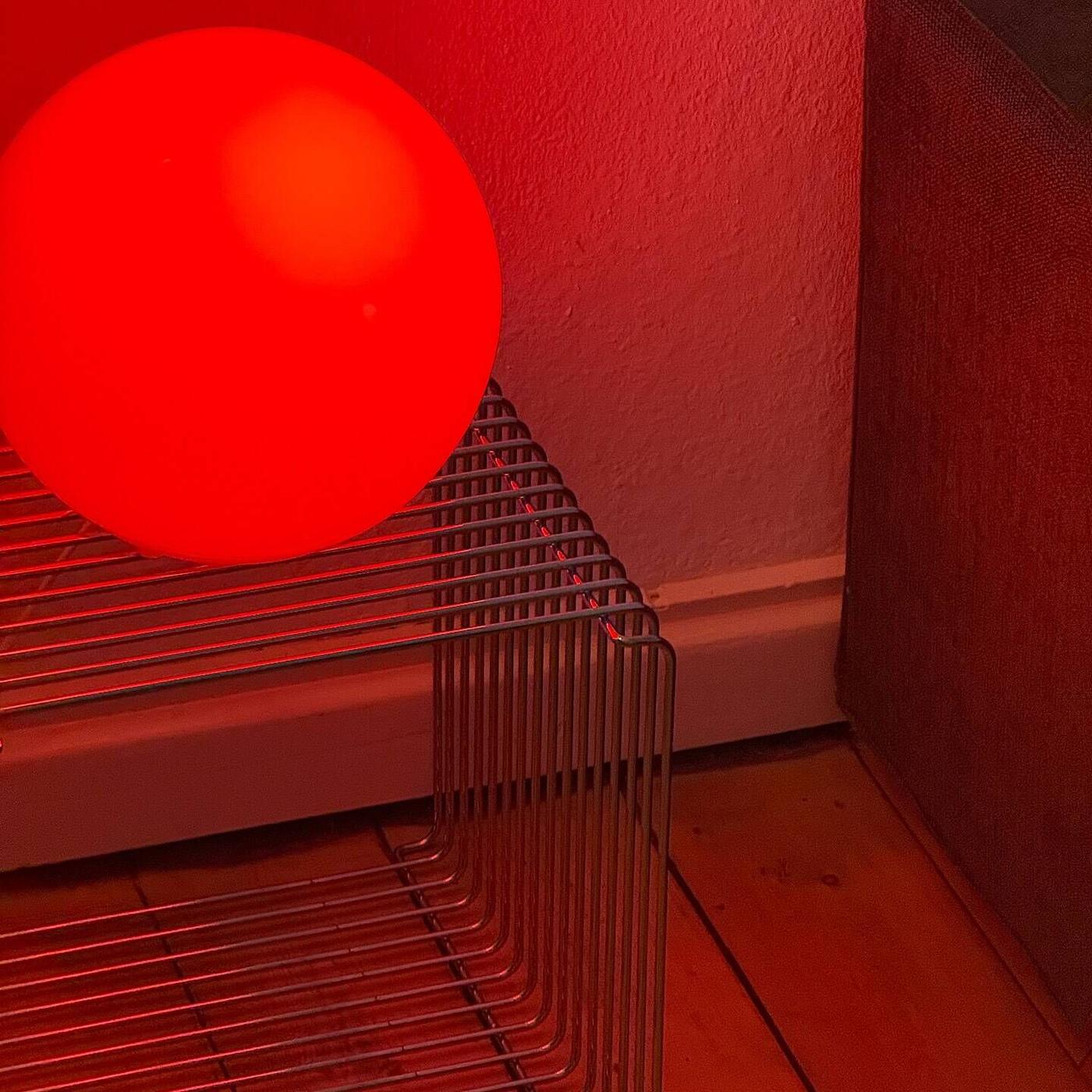 En FADO klotformad lampa står på ett genomskinligt, rutmönstrat sidobord mot ett hörn av ett rum med trägolv.