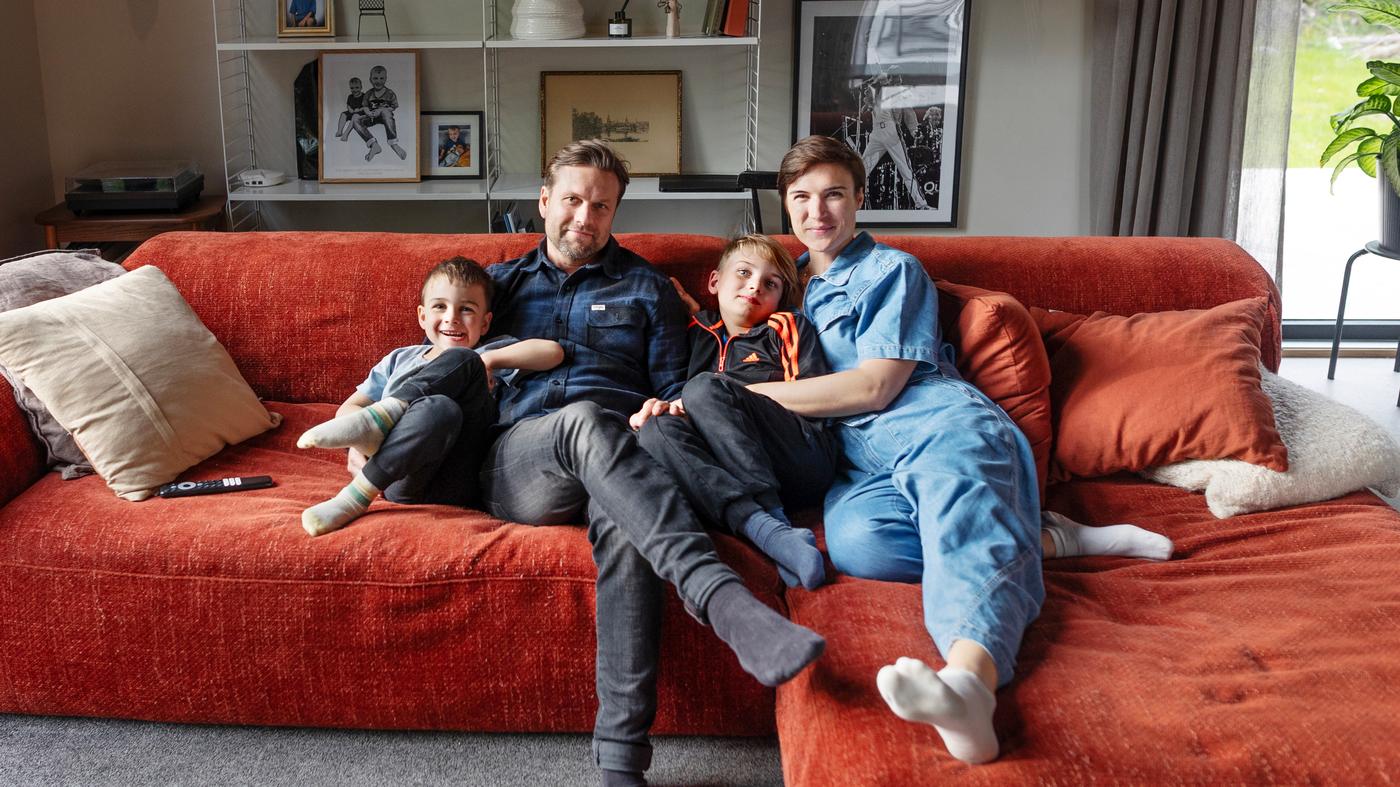 En familj med två vuxna och två barn sitter i en röd soffa.