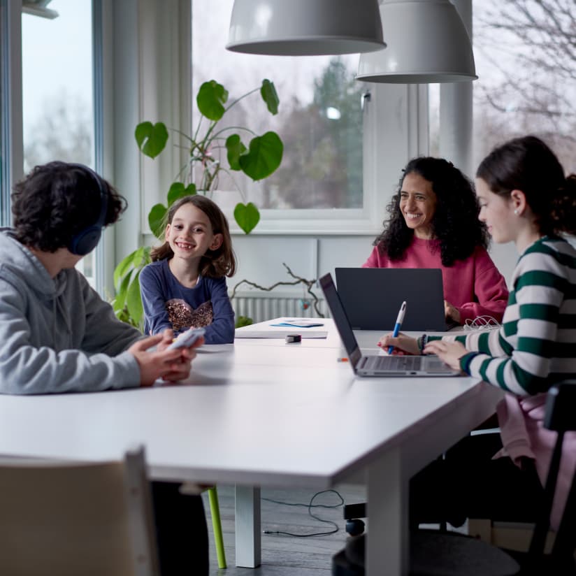 En familj samlad runt ett bord med två personer som arbetar framför varsin dator.