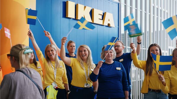En flok IKEA medarbejdere med gule trøjer står på en gul løber og flager til åbningen af IKEA København med det svenske flag.