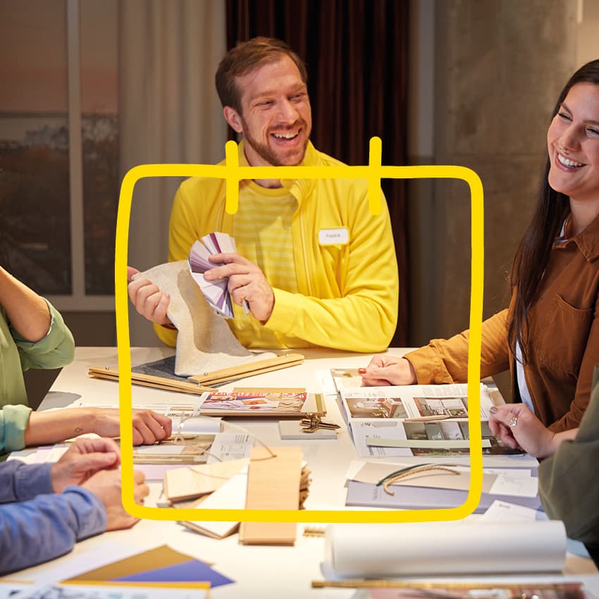 En glad IKEA medarbetare sitter runt ett bord och håller en workshop med några IKEA Family medlemmar.