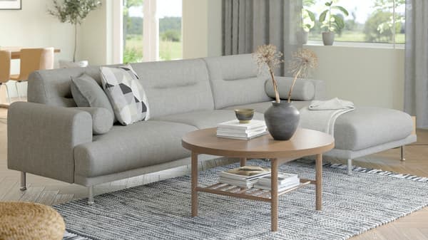 En grå LÅNGARYD sofa med chaiselong står i en lys stue ved et sofabord af træ og en gråt og hvidt tæppe på gulvet.