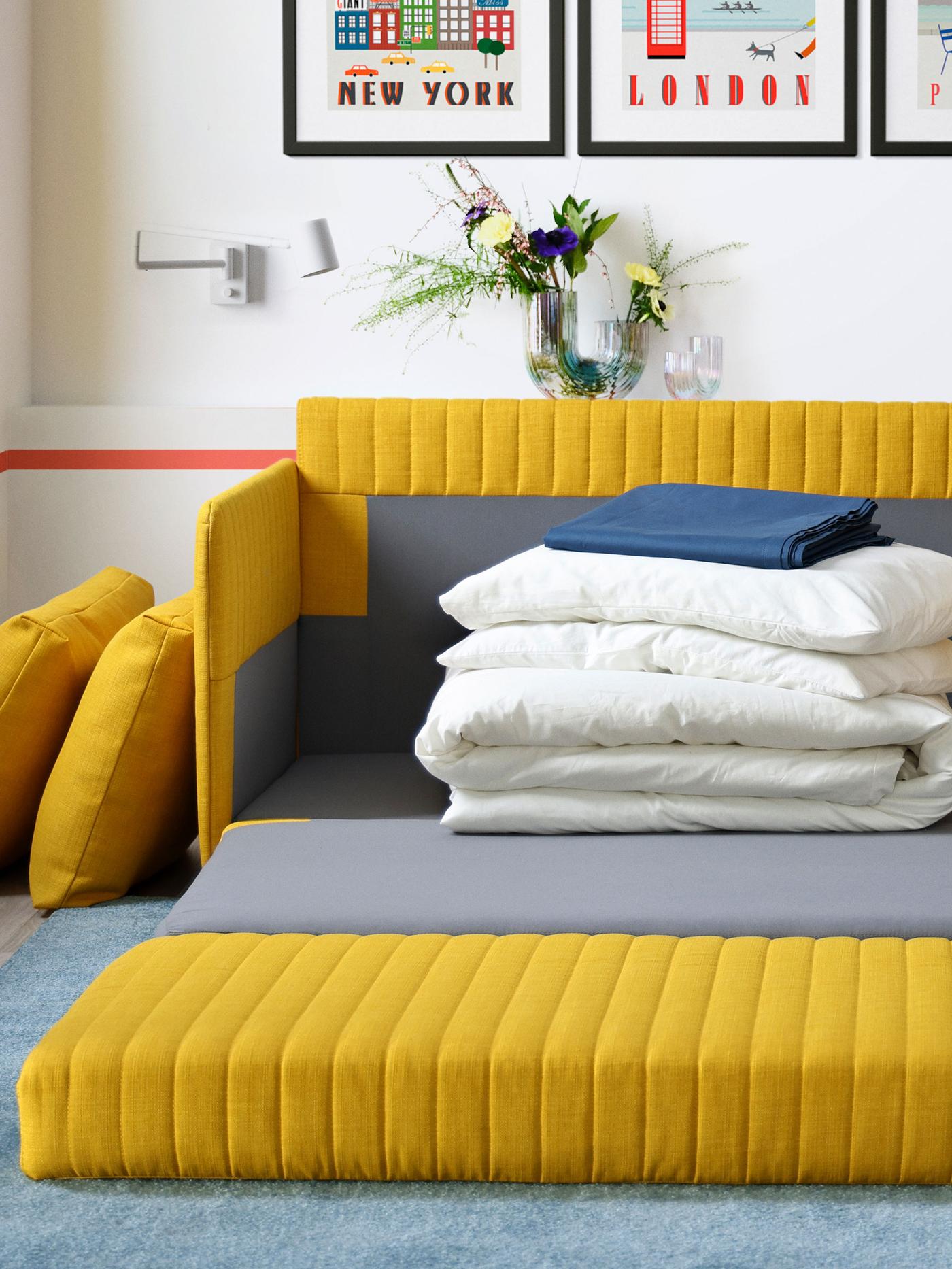 En gul bäddsoffa utbäddad i med vita täcken och kuddar staplade på varandra.