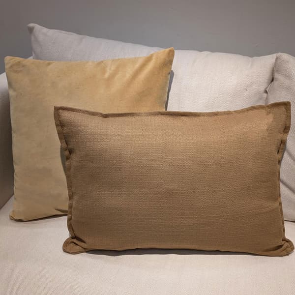 En gulbrun  sammetskudde till sammans med en brun rektangulär kudde i en ljusbeige soffa.
