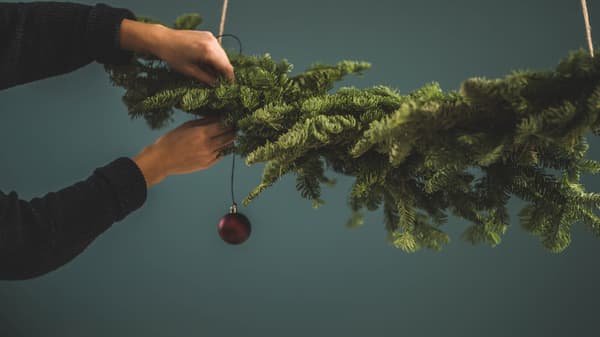 En hand hänger upp julgranskulor i en grön gren.