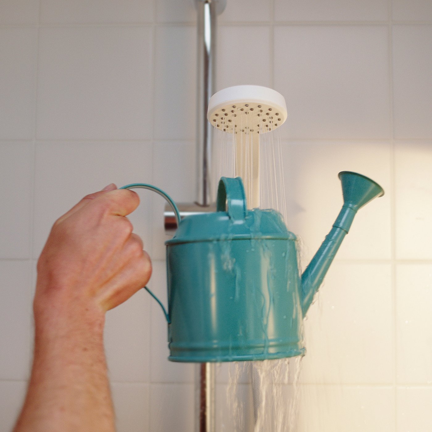 En hånd holder en lyseblå vandkande ind uner en hvid bruser som fylder vandkanen med vand.