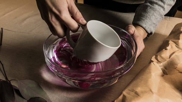En hand som doppar IKEA VÄRDERA mugg i en skål med vatten och nagellack. 