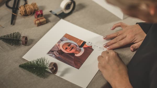 En hand som limmar på snögubben på passpartoun och sätter in fotografiet.  