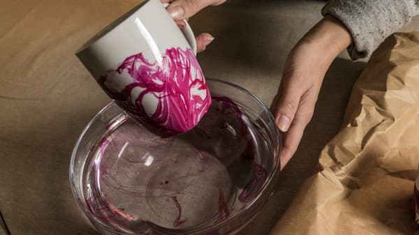En hand som lyft upp IKEA VÄRDERA mugg ur vattnet och visar hur nagellacket har fastnat på muggen. 