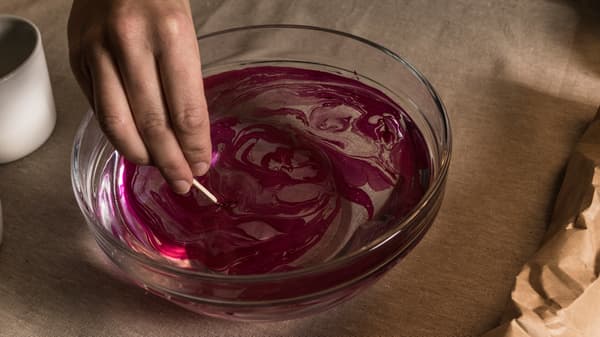 En hand som rör runt i en skål med vatten och nagelllack med en tandpetare. 