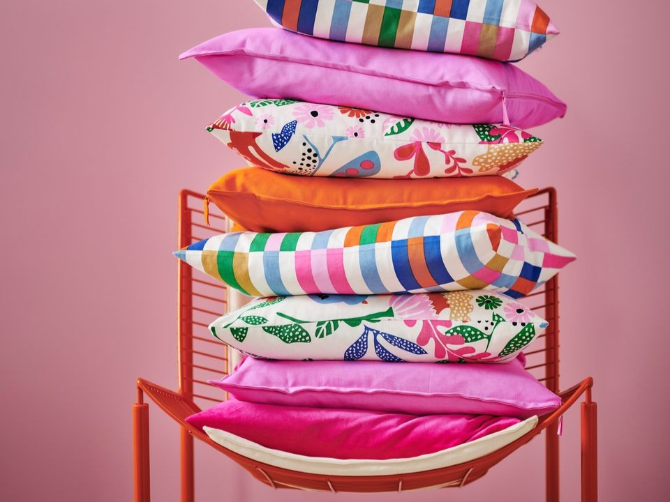 En hög med färgglada kuddar ligger på en orange stol.