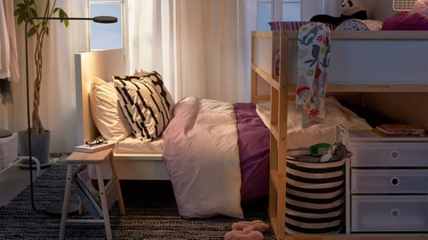 En højseng er placeret hen over en lavere seng i et lille soveværelse, hvor barnet sover i højsengen og forældrene i dobbeltsengen.
