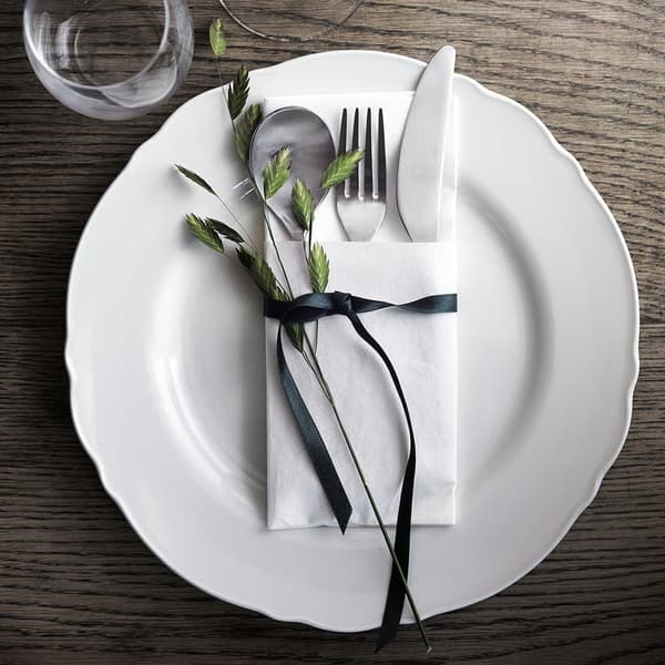 En hvid UPPLAGA tallerken ses på et bord med bestik og en hvid serviet 