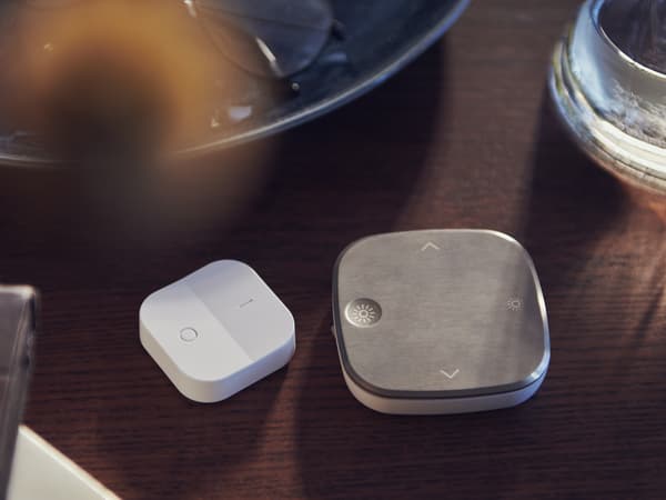 En hvit TRÅDFRI trådløs dimmer, en STYRBAR fjernkontroll og et glass vann på brunt bord.